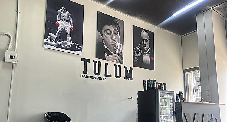 Pared blanca con retratos en blanco y negro y el letrero TULUM Barber Shop en relieve