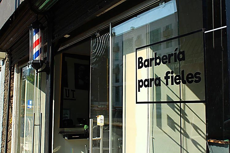Entrada de cristal de Tulum Barbershop con el vinilo «Barbería para fieles» y el poste de barbero a un lado