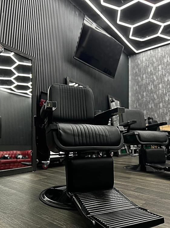 Sillón de barbero de cuero negro bajo el techo de luces hexagonales y el muro de lamas negras